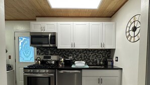 A modern kitchen with white cabinets, stainless steel appliances, a microwave, and a clock on the wall.