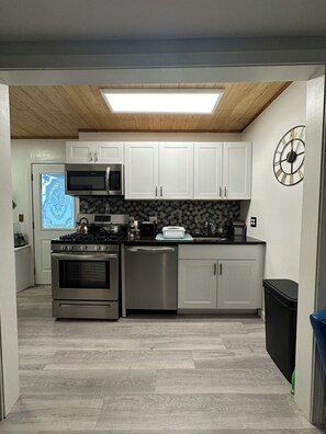 Una cocina moderna con armarios blancos, electrodomésticos de acero inoxidable, un microondas y un reloj en la pared.