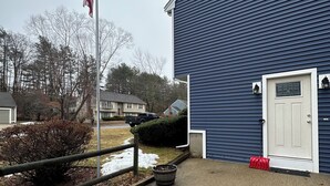 A building with a blue exterior, a flagpole with an American flag, a door with a window, and a red object on the ground.