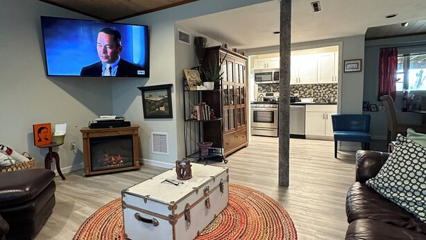 A living room with a television, a fireplace, a kitchen in the background, and a brown leather couch.
