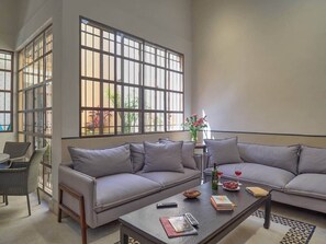 A spacious living room with a large window, a grey sofa, a coffee table with books and a remote control, and a small side table with a vase. - Casa Isabela Amazing Architecture in Merida Centro (Mérida)