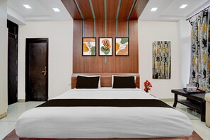 A hotel room with a large bed, a wooden headboard, a wall-mounted artwork, a curtain, and a small table with a cup and saucer. - Classic Rainbow Gold Inn (Lucknow)