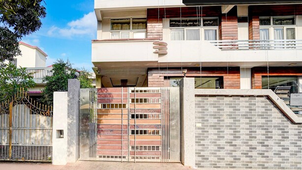 Uma casa moderna de dois andares, com portão fechado, varanda e escada que leva ao andar superior.