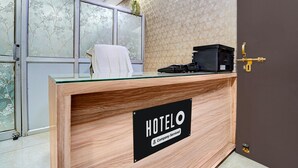 Een hotel receptiebalie met een 'HOTELO' bord, een glazen blad en een kleine plant erop.
