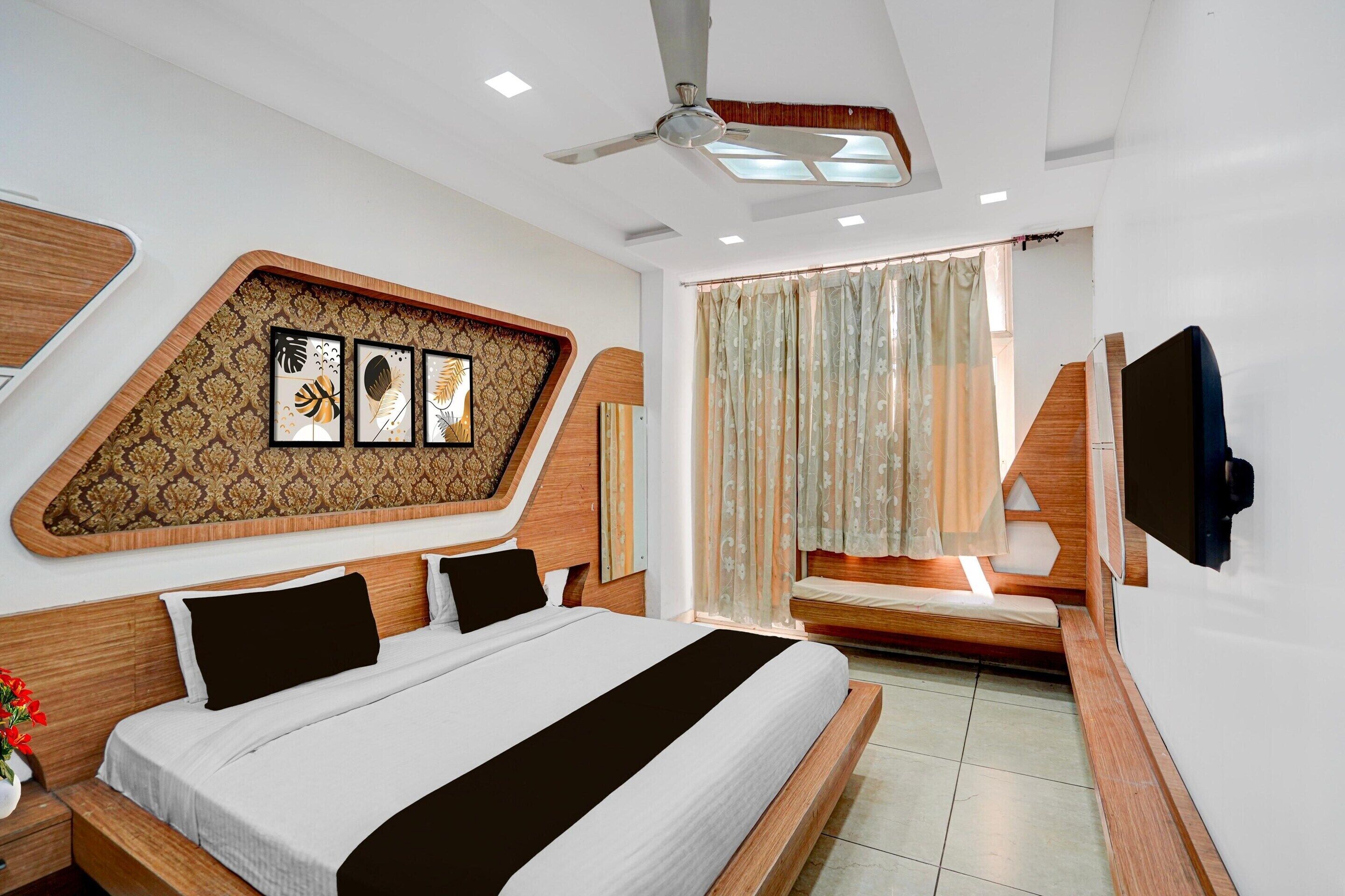 Une chambre d’hôtel moderne avec un grand lit, un ventilateur de plafond, une télévision et une fenêtre avec des rideaux.