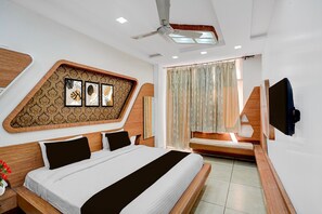 A modern hotel room with a large bed, a ceiling fan, a TV, and a window with curtains. - Classic Rainbow Gold Inn (Lucknow)
