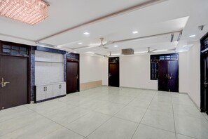 A spacious room with a tiled floor, ceiling fans, recessed lighting, and dark wooden doors. - Classic Rainbow Gold Inn (Lucknow)