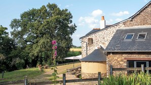A stone building with a sloped roof, a wooden fence, and a picnic table. - La Hulotte en Brocéliande - Yoga, seminars & group holidays 15 pers. (Saint-Malon-sur-Mel)