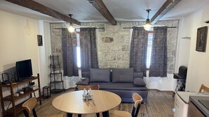 Una sala de estar con una pared de piedra, un sofá, una mesa de comedor con sillas, un televisor y un refrigerador pequeño.