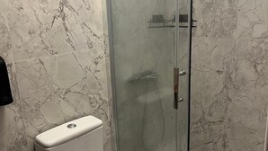 Un baño con inodoro, ducha con cerramiento de vidrio y paredes de mármol.