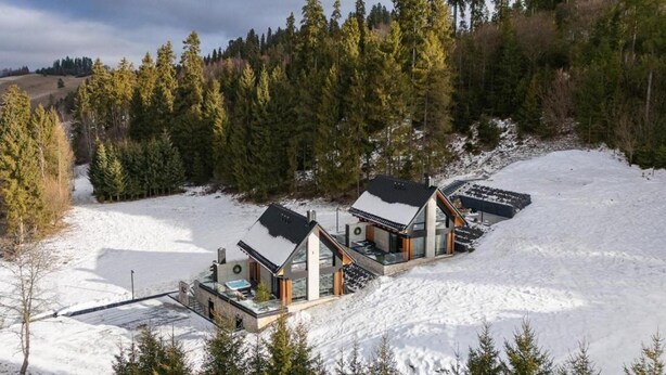 Een moderne cabin met een glazen gevel, omgeven door besneeuwde vlaktes en een dicht bos.