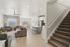 A modern living room with a sofa, a dining area, a kitchen with a bar, and a staircase. - Family Escape Near Zion, Pool, Private Hot Tub/Patio (Hurricane)
