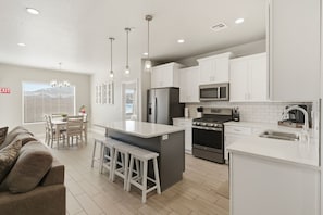 A modern kitchen with white cabinets, a central island with stools, stainless steel appliances, and pendant lighting. - Family Escape Near Zion, Pool, Private Hot Tub/Patio (Hurricane)