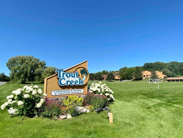 Schild für Trout Creek Condominium Resort & Vacation Rentals mit einer Wiese und Bäumen im Hintergrund.