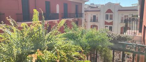 Une cour bordée de bâtiments rouges, avec un balcon et de la verdure.