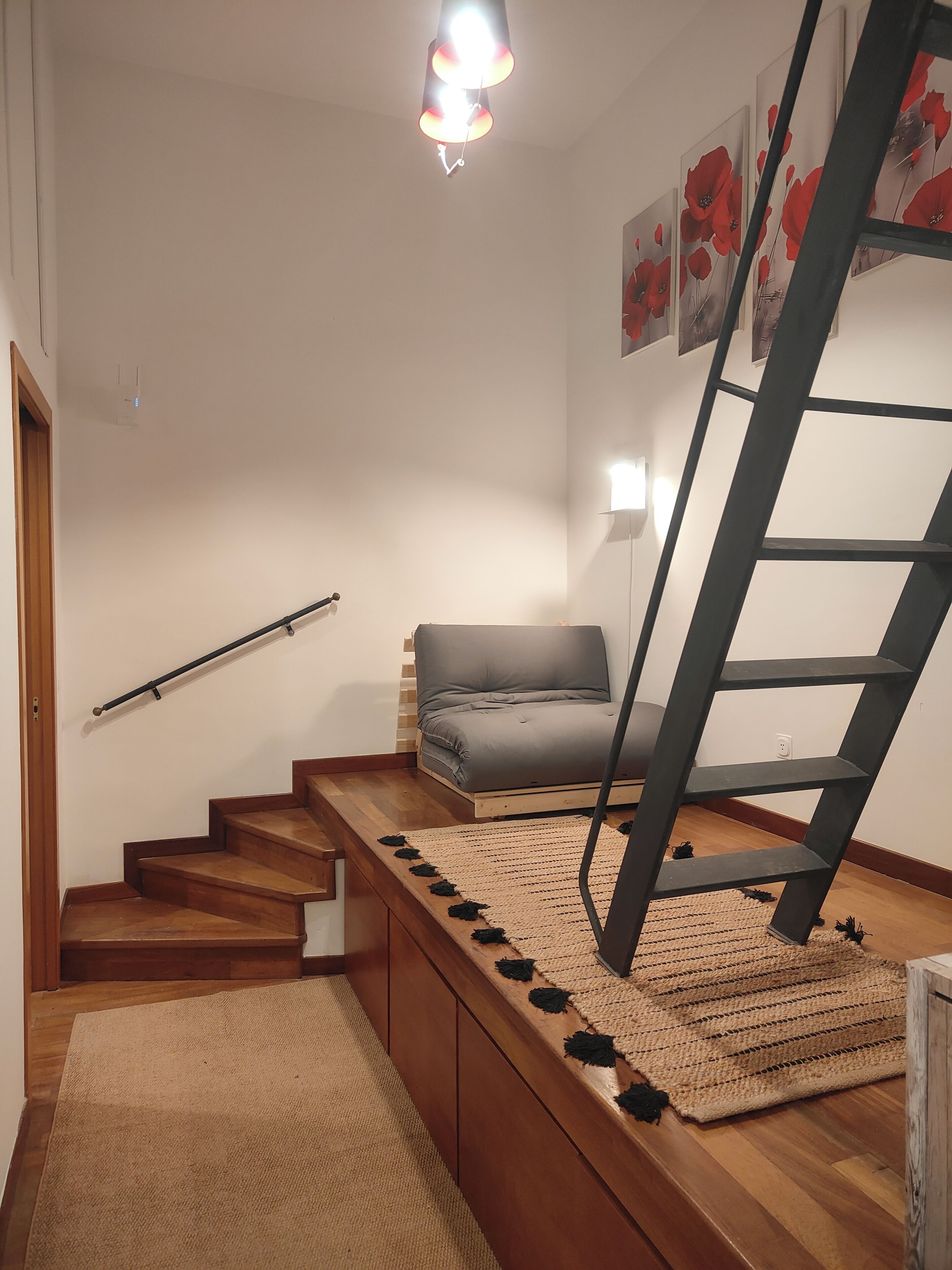 Un escalier avec des marches recouvertes de bois, un canapé gris et une échelle noire.