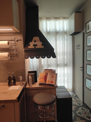 A compact kitchen with a built-in stove, a bar stool, and a window with sheer curtains. - Amapola House Bari (Bari)