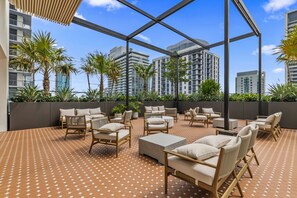 A rooftop patio with outdoor furniture, palm trees, and a view of high-rise buildings. - The Crosby | King Suite + Rooftop Pool (Miami)