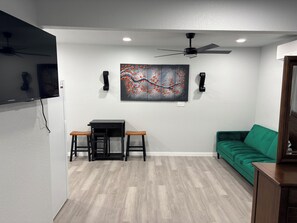 A room with a green sofa, a black table with two stools, a ceiling fan, and a wall-mounted painting. - Modern 1-bedroom studio in fabulous Fort Worth (Fort Worth)
