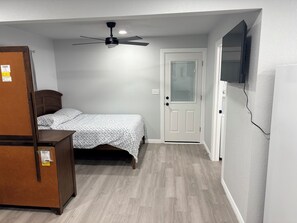 A bedroom with a bed, a ceiling fan, a door, and a television mounted on the wall. - Modern 1-bedroom studio in fabulous Fort Worth (Fort Worth)