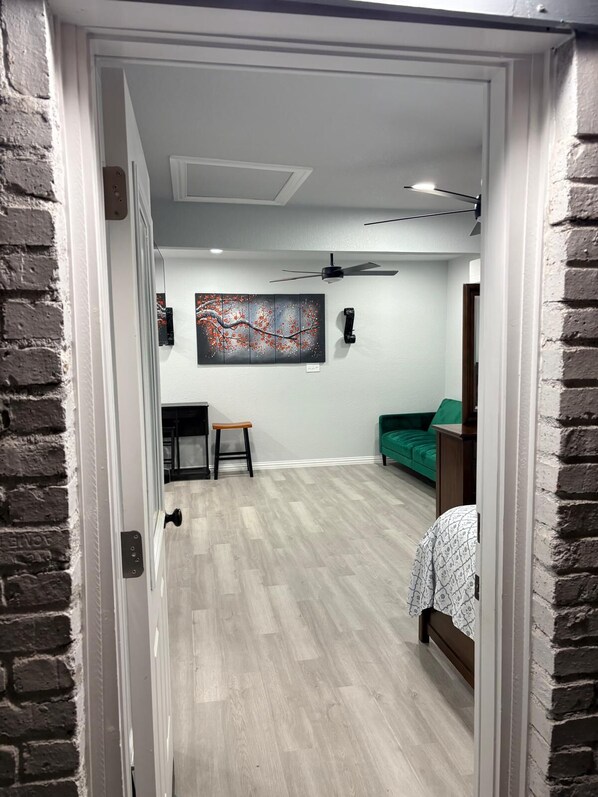 A room with a wooden floor, a green sofa, a small stool, a ceiling fan, and a wall-mounted artwork. - Modern 1-bedroom studio in fabulous Fort Worth (Fort Worth)