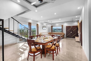 A spacious dining area with a large wooden table, multiple chairs, and a view of the outdoors. - Unique Farmhouse by ELIVAAS (Noida)