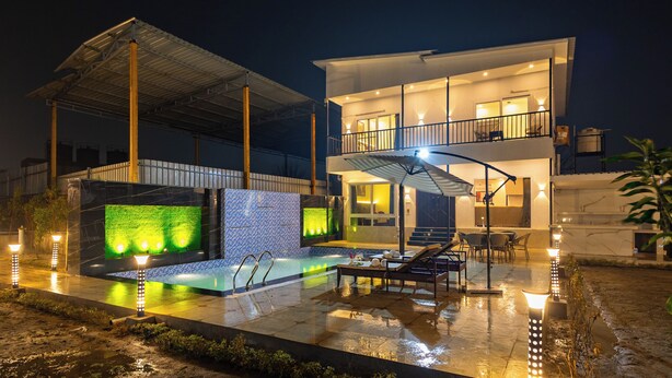 Ein modernes, zweistöckiges Haus mit Swimmingpool, Sitzgelegenheiten im Freien und einer überdachten Terrasse.
