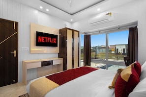 A modern hotel room with a large bed, a TV mounted on the wall, a balcony with a pool view, and a door with a handle. - Unique Farmhouse by ELIVAAS (Noida)