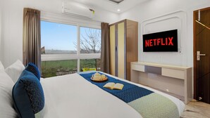 Ein Hotelzimmer mit Bett, Fernseher, Fenster mit Vorhängen und Blick ins Freie.
