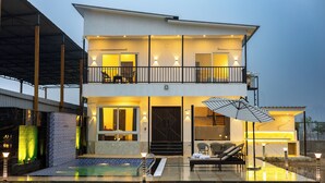 Ein modernes Haus mit zwei Etagen, einem Balkon, einem Swimmingpool und Sitzgelegenheiten im Freien.