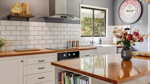 Una cucina moderna con mobili bianchi, un piano di lavoro in legno, forno integrato, una finestra con vista e una sveglia appesa al muro.