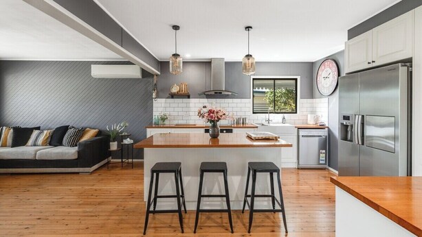 Una cucina moderna con isola centrale, sgabelli da bar, forno integrato e frigorifero in acciaio inossidabile.