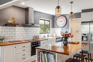 Une cuisine moderne avec des meubles blancs, un plan de travail en bois, un îlot central et une grande horloge murale.