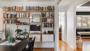 Una stanza con una libreria in legno piena di libri, una scrivania con un computer e un tavolo da pranzo con sedie.