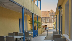 A courtyard with outdoor seating, a potted plant, and a building with a tiled roof in the background. - Hôtel Restaurant Le Plat d'étain (Brou)