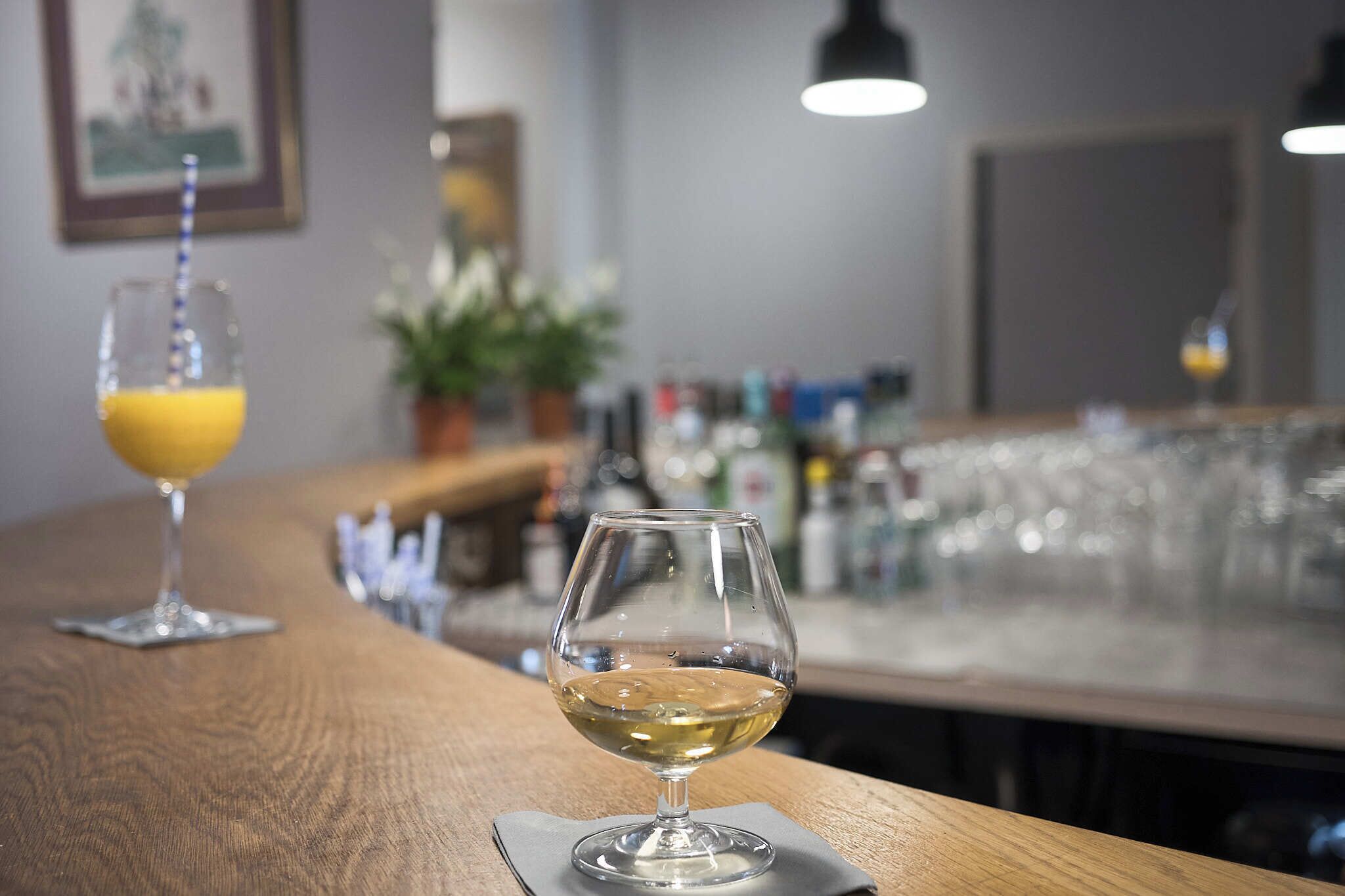 Zona de bar con una copa de vino blanco y un vaso de zumo de naranja sobre la barra.