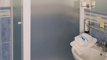A bathroom with a glass shower enclosure, a sink, a trash bin, and a mirror with a towel on it.