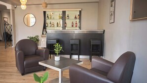 A modern living room with leather sofas, a coffee table, and a bar area with shelves of bottles. - Hôtel Restaurant Le Plat d'étain (Brou)