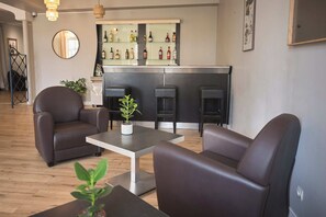 A modern living room with leather sofas, a coffee table, and a bar area with shelves of bottles.