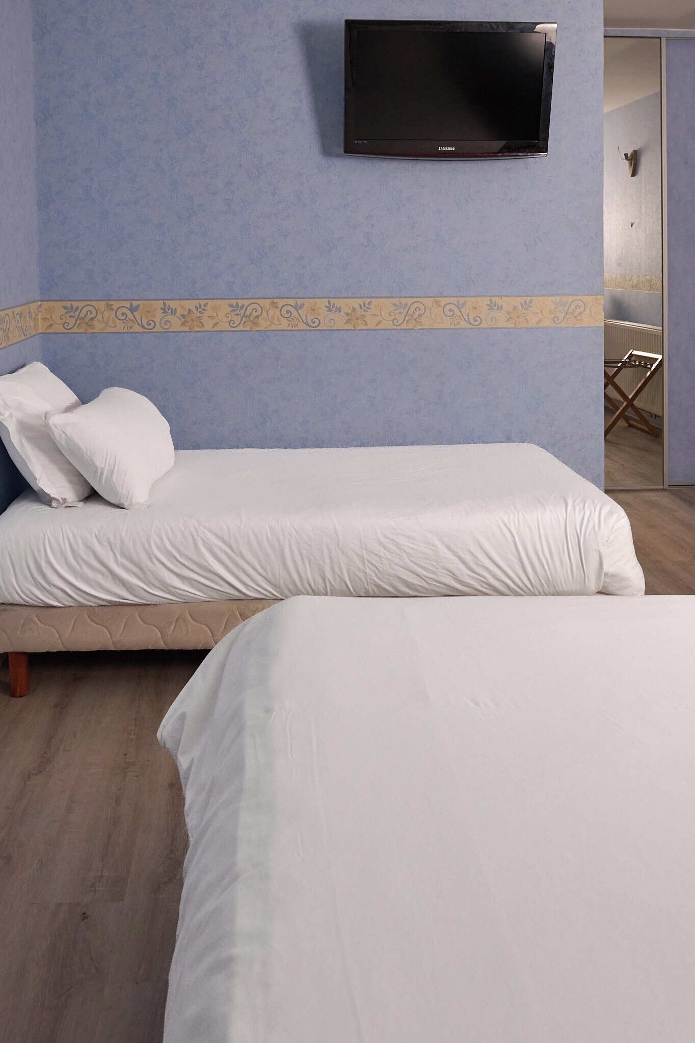 A room with two beds, a flat-screen TV mounted on the wall, and a patterned border on the wall.