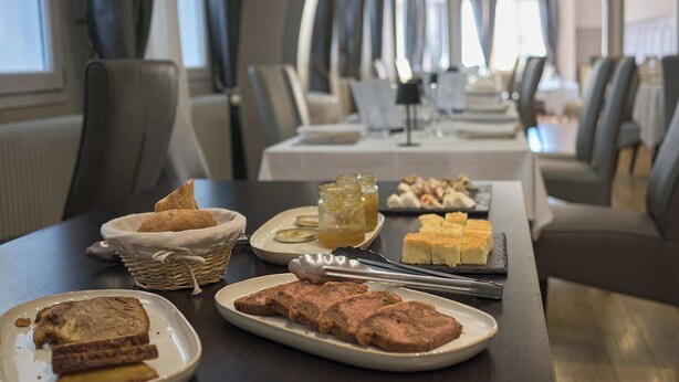 A dining area with tables set for meals, including bread, pastries, and a meat dish. - Hôtel Restaurant Le Plat d'étain (Brou)