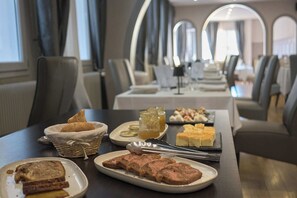 A dining area with tables set for meals, including bread, pastries, and a meat dish. - Hôtel Restaurant Le Plat d'étain (Brou)