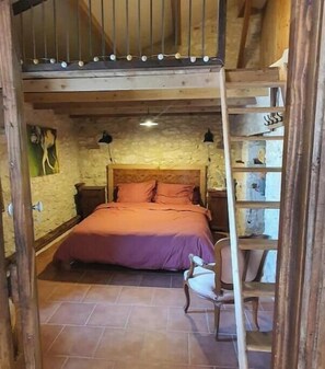Una camera da letto rustica con un letto di legno, una sedia, una scala e un muro in pietra.