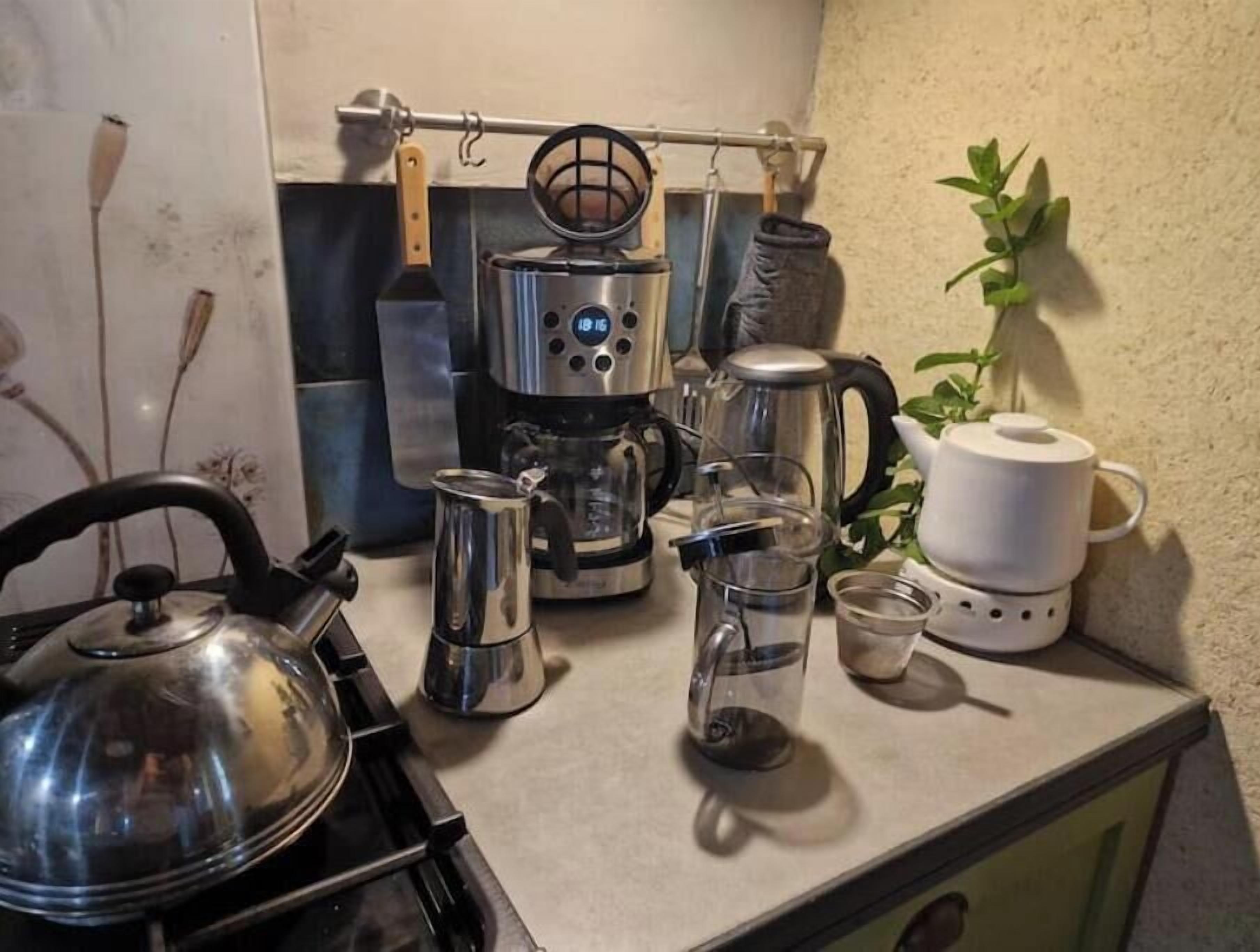 Une cuisine équipée d’une cuisinière, d’une bouilloire, d’une machine à café et de divers récipients.