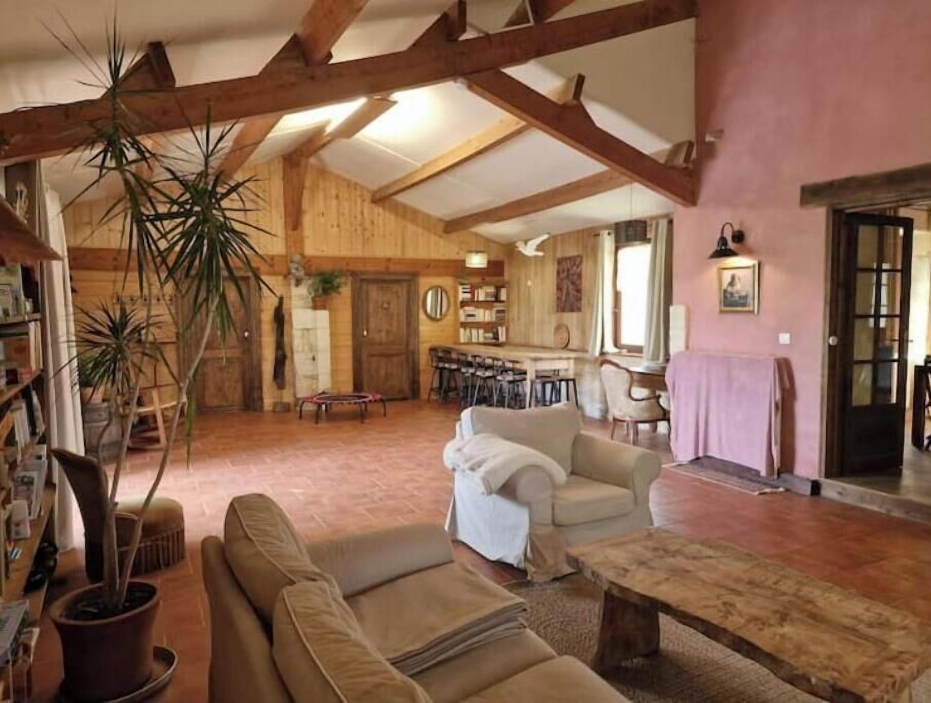 A rustic interior with exposed wooden beams, a sofa, a coffee table, and a dining area with chairs.