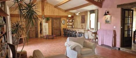 A rustic interior with exposed wooden beams, a sofa, a coffee table, and a dining area with chairs.