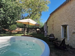 Una vasca idromassaggio in un giardino sul retro, con un'amaca, un ombrellone da patio e un edificio in pietra.