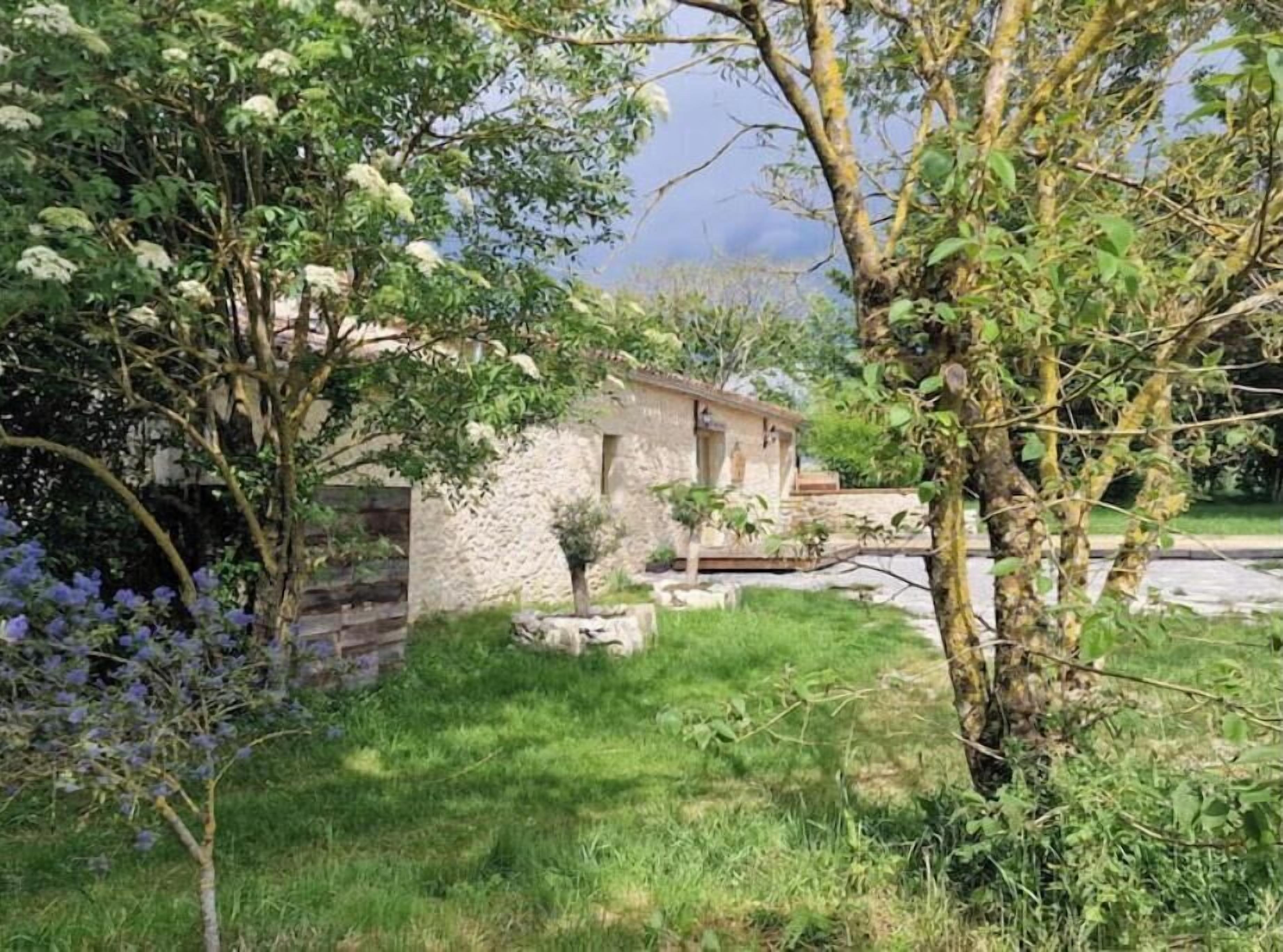 Un edificio de piedra rústico con un pequeño jardín, rodeado de árboles y arbustos.
