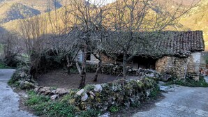 Um edifício rústico de pedra com telhado de telhas, rodeado por árvores sem folhas e uma parede de pedra.