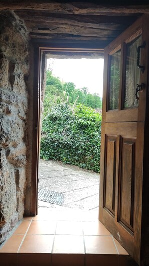 Une porte en bois rustique donne sur un espace pavé, bordé d’un côté par un mur de pierres.